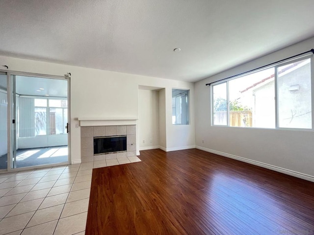 unfurnished living room featuring a healthy amount of sunlight, a tiled fireplace, and light hardwood / wood-style flooring