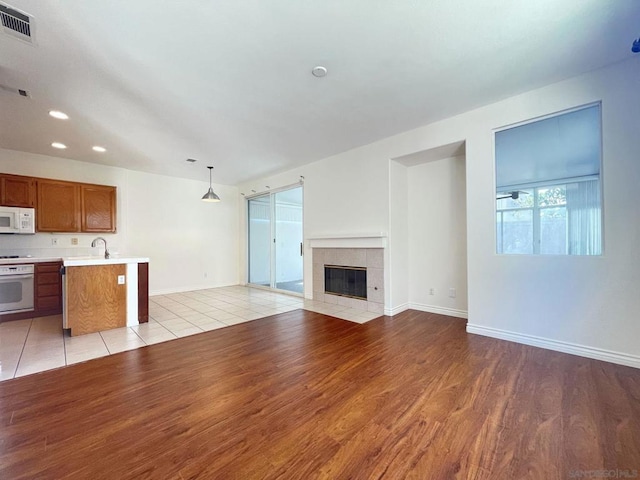 unfurnished living room featuring light wood-type flooring, a tiled fireplace, and sink