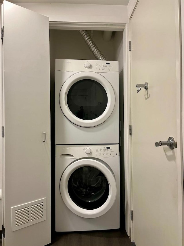 laundry room featuring dark wood-type flooring and stacked washer / dryer