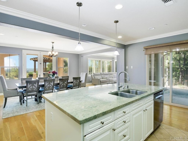 kitchen with light stone countertops, sink, crown molding, and an island with sink