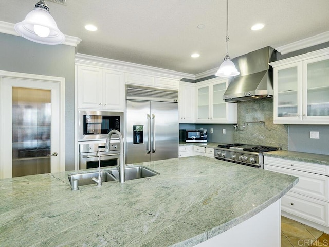 kitchen with decorative light fixtures, white cabinets, built in appliances, and range hood