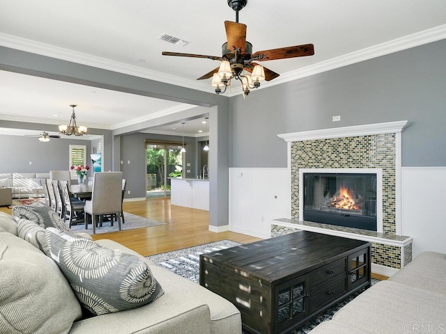 living room with a fireplace, ceiling fan with notable chandelier, ornamental molding, and hardwood / wood-style flooring