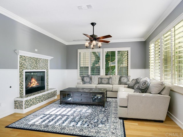 living room with ceiling fan, a tile fireplace, crown molding, and light wood-type flooring