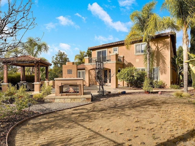 rear view of house with a gazebo, an outdoor fireplace, a balcony, and a patio