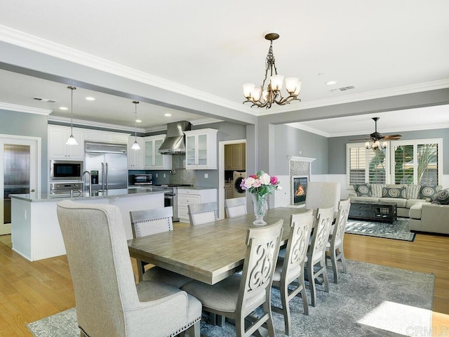 dining room featuring ceiling fan with notable chandelier, washer / clothes dryer, sink, ornamental molding, and light wood-type flooring