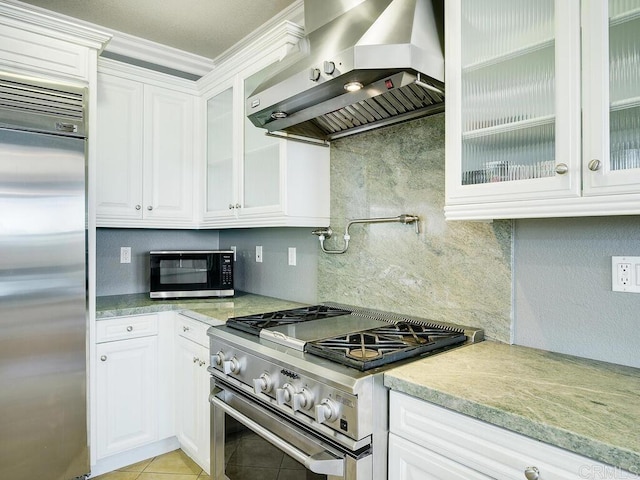 kitchen featuring white cabinetry, wall chimney range hood, high end appliances, decorative backsplash, and light tile patterned flooring