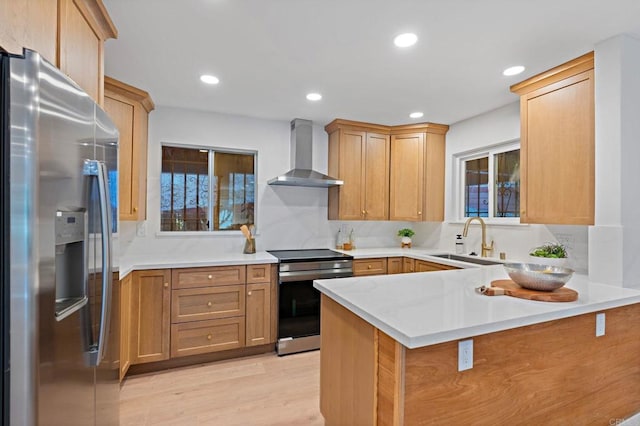 kitchen featuring appliances with stainless steel finishes, wall chimney exhaust hood, light hardwood / wood-style floors, sink, and kitchen peninsula