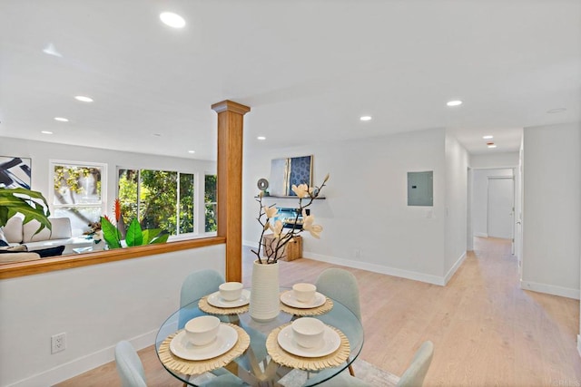 dining room featuring decorative columns, electric panel, and light wood-type flooring