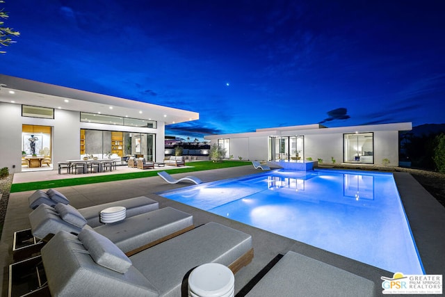 pool at night featuring an outdoor living space and a patio