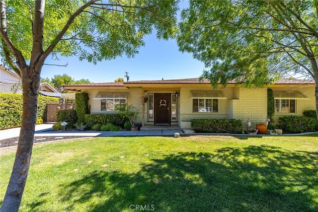 single story home featuring brick siding, a front lawn, stucco siding, and fence