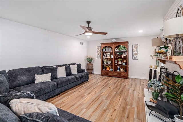 living room with ceiling fan, light hardwood / wood-style flooring, and a brick fireplace