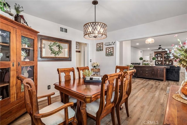 dining room with ceiling fan with notable chandelier and light hardwood / wood-style floors