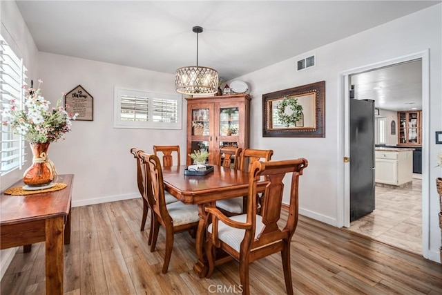 dining space featuring baseboards, an inviting chandelier, visible vents, and light wood-type flooring