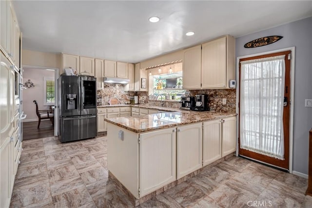 kitchen featuring tasteful backsplash, kitchen peninsula, stainless steel fridge with ice dispenser, and light stone counters