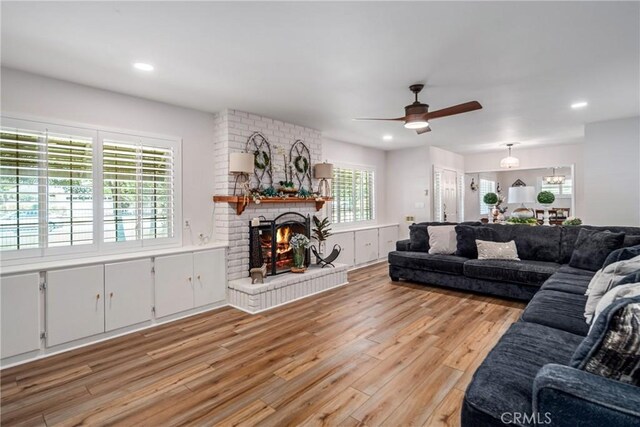 living room with ceiling fan, light hardwood / wood-style flooring, and a brick fireplace