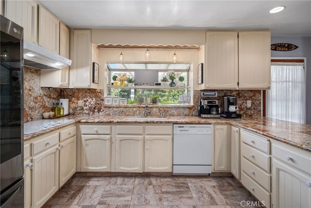 kitchen featuring white dishwasher, tasteful backsplash, a sink, and cream cabinetry