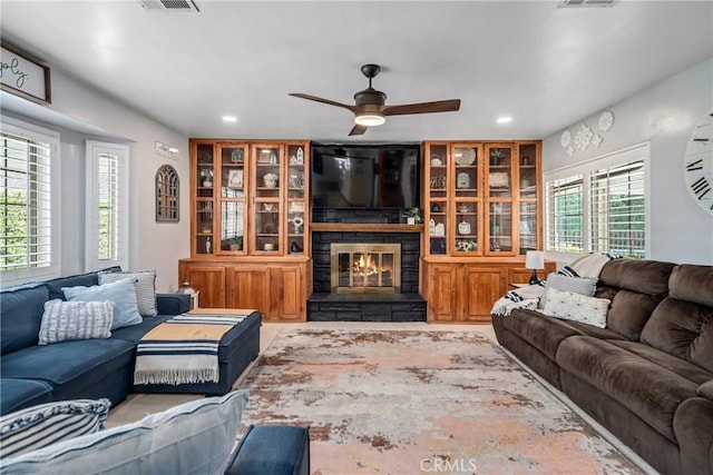 living area featuring a stone fireplace, recessed lighting, ceiling fan, and visible vents