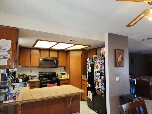 kitchen featuring sink, a textured ceiling, tile counters, kitchen peninsula, and black appliances