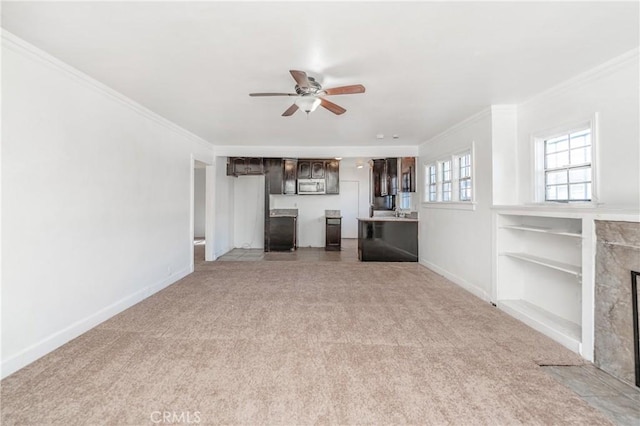 unfurnished living room featuring built in shelves, light colored carpet, ceiling fan, and crown molding