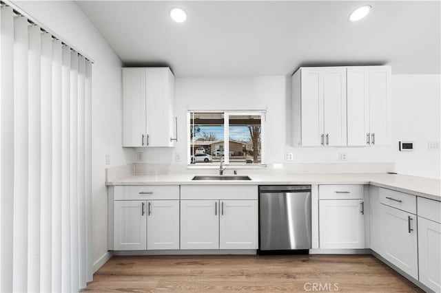 kitchen with stainless steel dishwasher, light wood-type flooring, sink, and white cabinetry