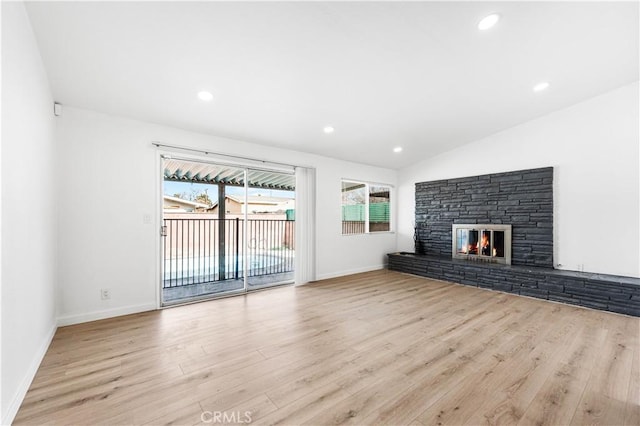 unfurnished living room with light wood-type flooring, lofted ceiling, and a stone fireplace