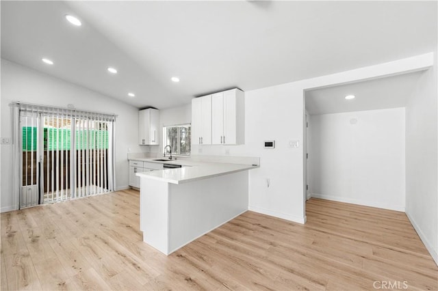 kitchen with lofted ceiling, kitchen peninsula, white cabinetry, and light hardwood / wood-style floors