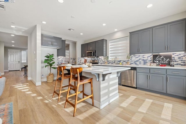 kitchen featuring appliances with stainless steel finishes, gray cabinetry, a kitchen island, light hardwood / wood-style flooring, and sink