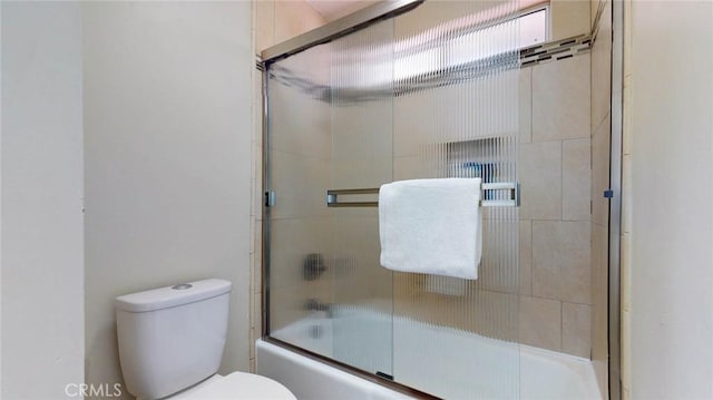 bathroom featuring toilet and bath / shower combo with glass door