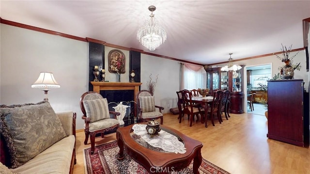 living room with a large fireplace, light hardwood / wood-style flooring, ornamental molding, and a notable chandelier