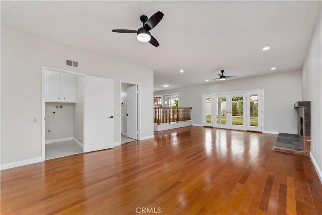 unfurnished living room with ceiling fan, french doors, a tile fireplace, and hardwood / wood-style flooring