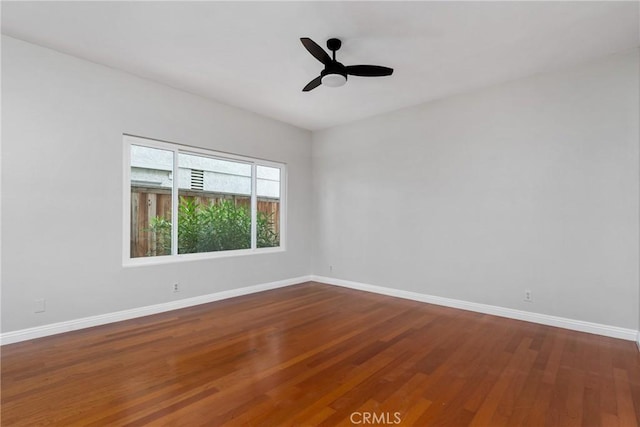 unfurnished room featuring dark wood-style flooring, ceiling fan, and baseboards