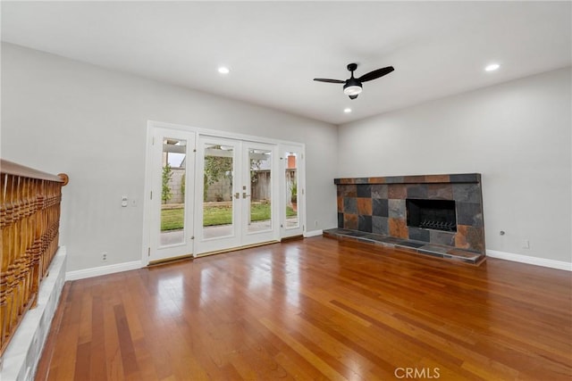 unfurnished living room featuring a ceiling fan, baseboards, a tiled fireplace, and wood finished floors