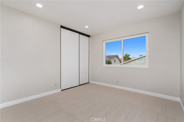 unfurnished bedroom featuring recessed lighting, a closet, light colored carpet, and baseboards