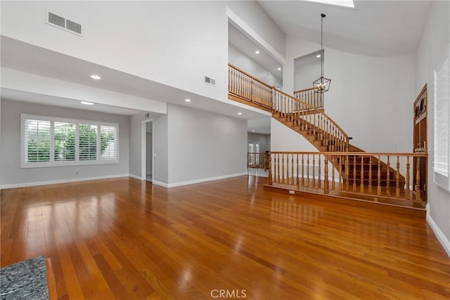 unfurnished living room featuring hardwood / wood-style floors, stairway, visible vents, and baseboards