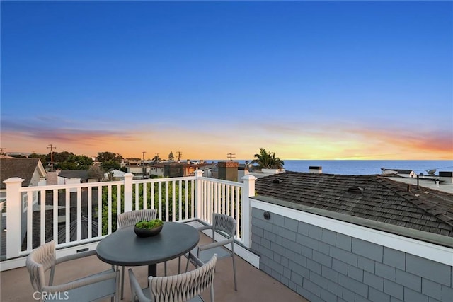 balcony at dusk featuring a water view