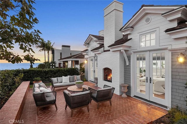 patio terrace at dusk with french doors and an outdoor living space with a fireplace