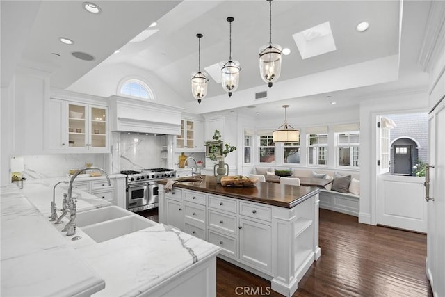 kitchen featuring dark stone countertops, double oven range, sink, hanging light fixtures, and white cabinets