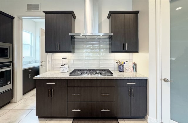 kitchen featuring decorative backsplash, appliances with stainless steel finishes, wall chimney range hood, and dark brown cabinets