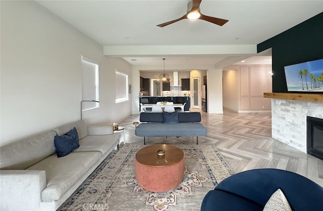 living room with light parquet floors, ceiling fan with notable chandelier, and a stone fireplace