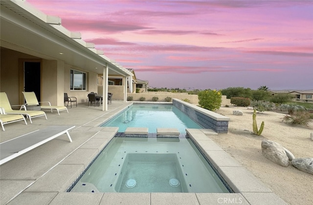 pool at dusk featuring a patio area and an in ground hot tub