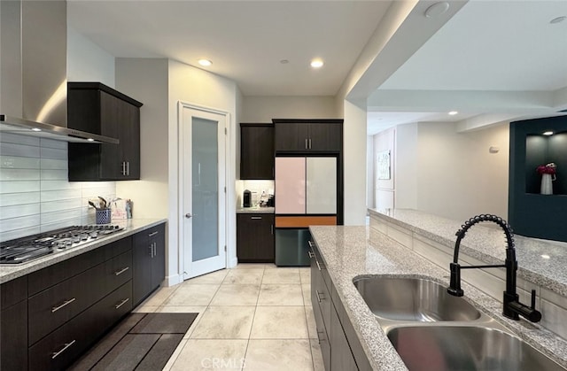 kitchen with stainless steel gas stovetop, tasteful backsplash, sink, light stone countertops, and wall chimney range hood