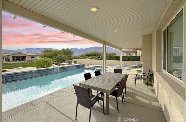 pool at dusk with an in ground hot tub, a mountain view, and a patio