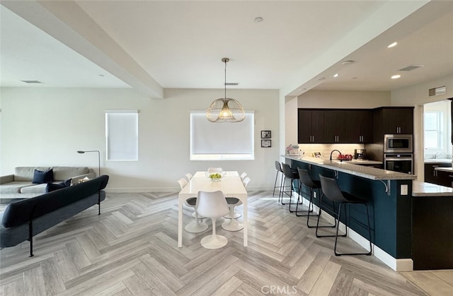 kitchen with light parquet floors, kitchen peninsula, a breakfast bar area, appliances with stainless steel finishes, and dark brown cabinets