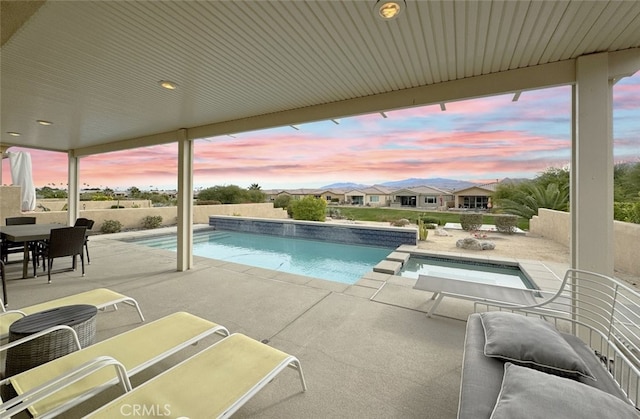 pool at dusk featuring a patio area and an in ground hot tub