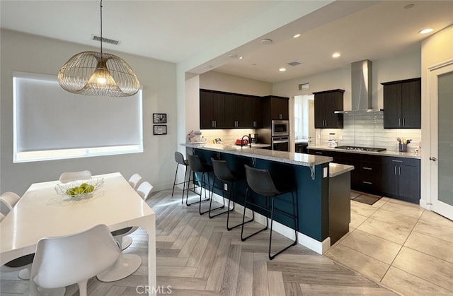 kitchen featuring appliances with stainless steel finishes, wall chimney exhaust hood, hanging light fixtures, kitchen peninsula, and a breakfast bar