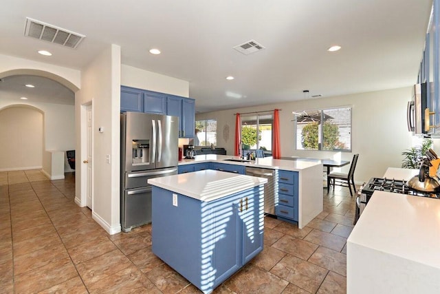 kitchen with kitchen peninsula, stainless steel appliances, blue cabinets, hanging light fixtures, and a center island