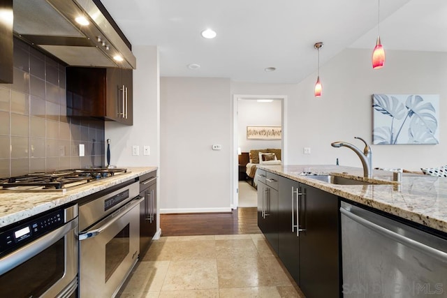 kitchen with light stone countertops, wall chimney exhaust hood, stainless steel appliances, sink, and hanging light fixtures