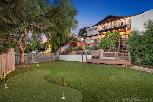 yard at dusk featuring a wooden deck and a balcony