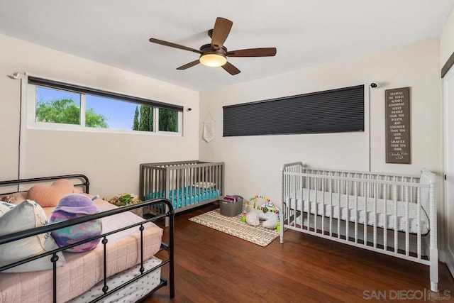 bedroom featuring a crib, dark hardwood / wood-style floors, and ceiling fan