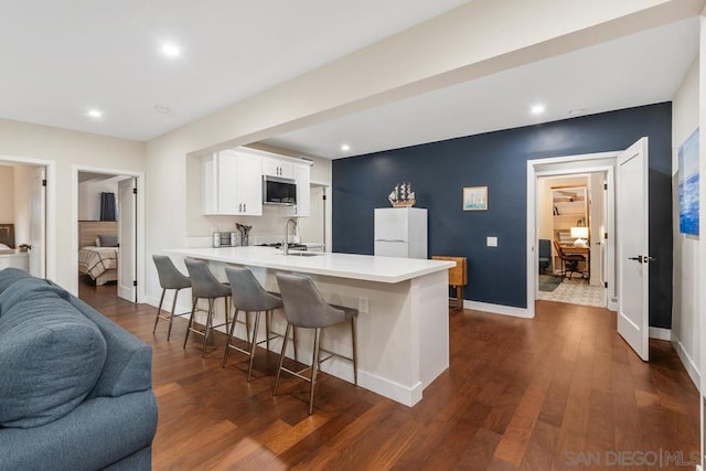 kitchen featuring white cabinets, dark hardwood / wood-style flooring, a kitchen bar, white fridge, and kitchen peninsula